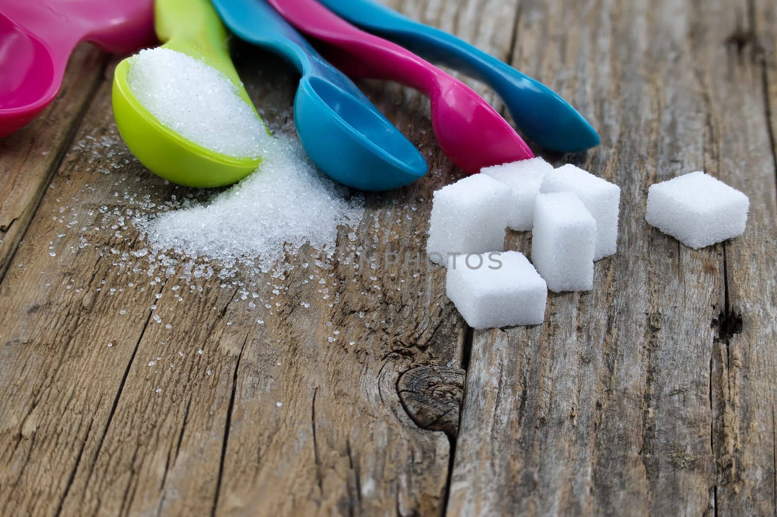 Sugar in colorful measuring spoons on wooden surface by NetPix