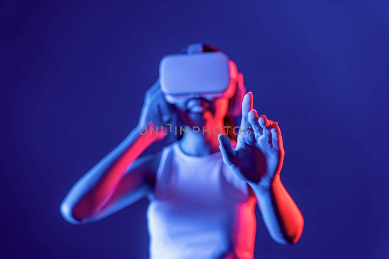 Smart female standing with surrounded by cyberpunk neon light wear VR headset connecting metaverse, futuristic cyberspace community technology. Woman using hand touching virtual object. Hallucination.