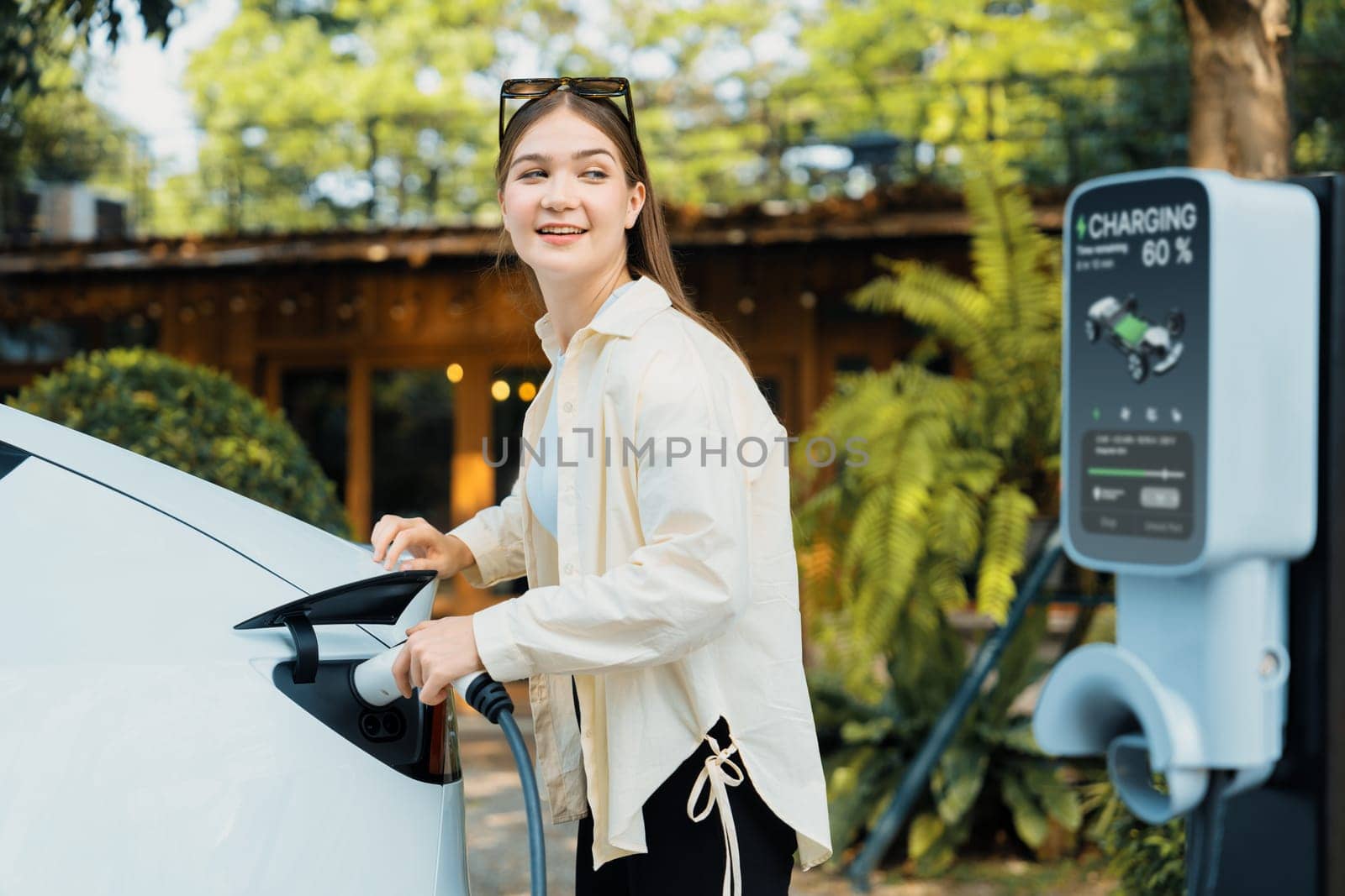 Young woman and sustainable urban commute with EV electric car recharging at outdoor cafe in springtime garden, green city sustainability and environmental friendly EV car. Expedient