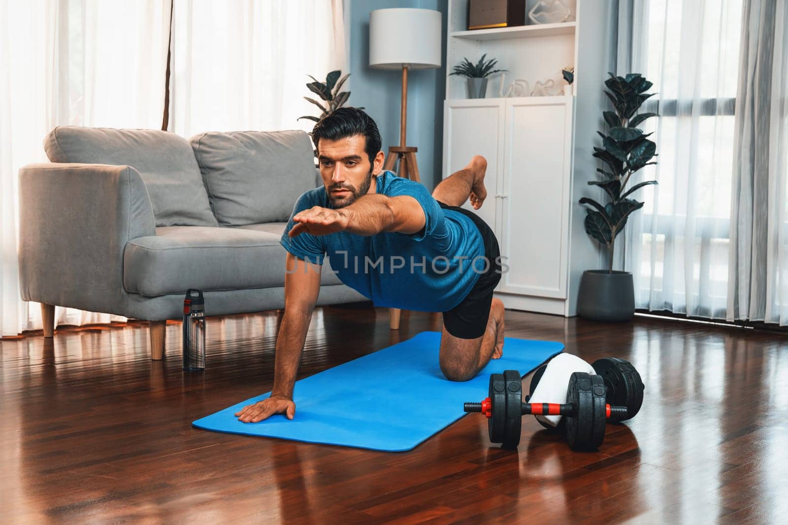 Flexible and dexterity man in sportswear doing yoga position in meditation posture on exercising mat at home. Healthy gaiety home yoga lifestyle with peaceful mind and serenity.