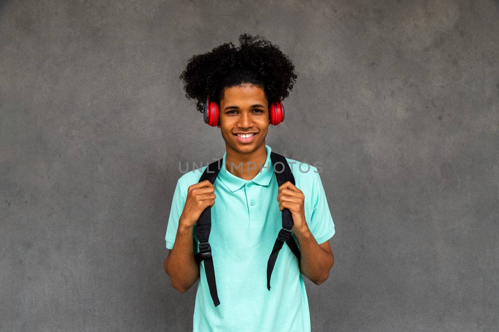 Happy teen African American boy with afro hairstyle looking at camera wearing headphones and backpack. by Hoverstock