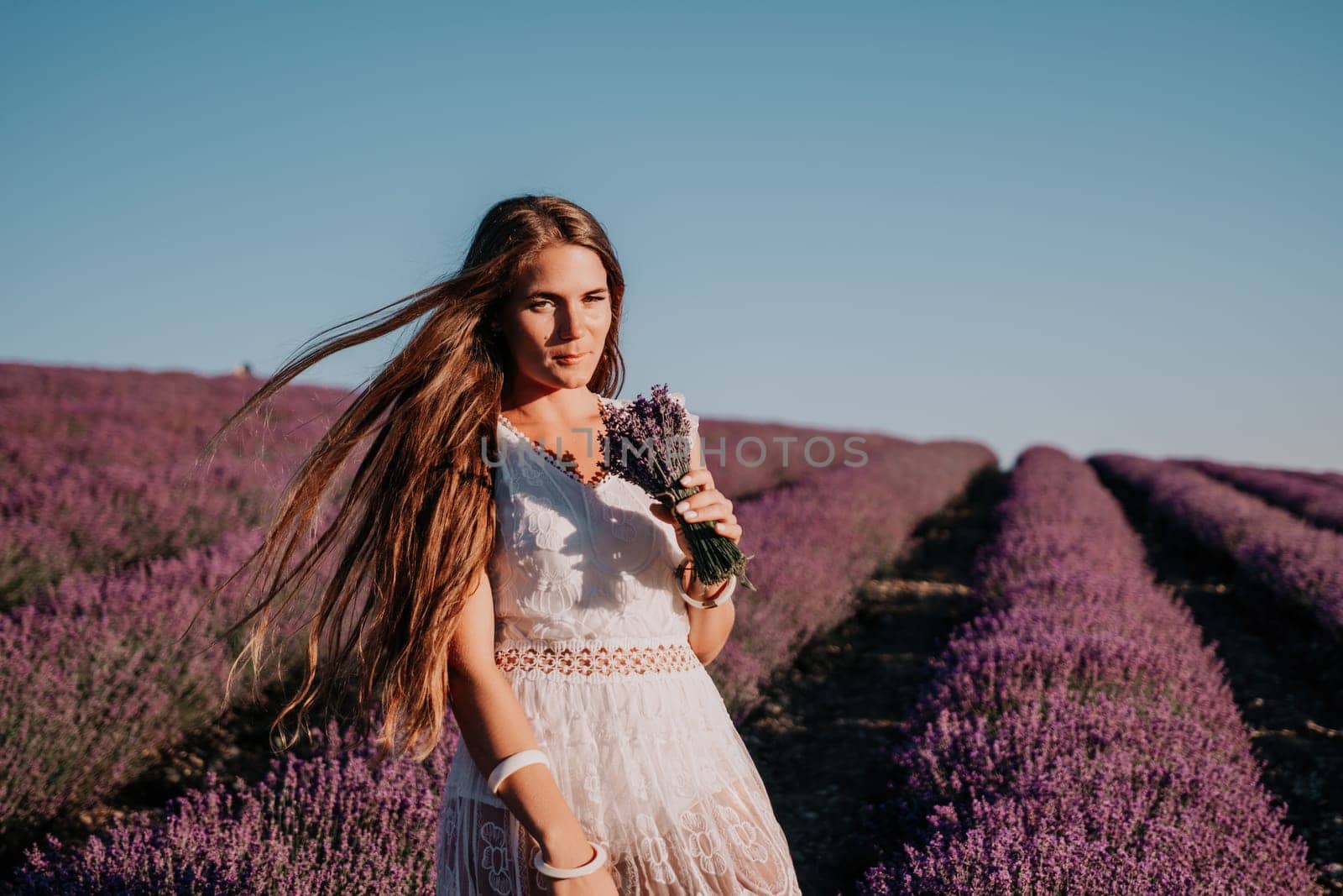 Woman lavender field. Happy carefree woman in a white dress walking in a lavender field and smelling a lavender bouquet on sunset. Ideal for warm and inspirational concepts in wanderlust and travel. by panophotograph