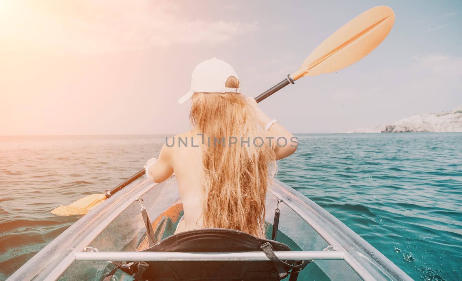 Woman in kayak back view. Happy young woman with long hair floating in transparent kayak on the crystal clear sea. Summer holiday vacation and cheerful female people having fun on the boat.