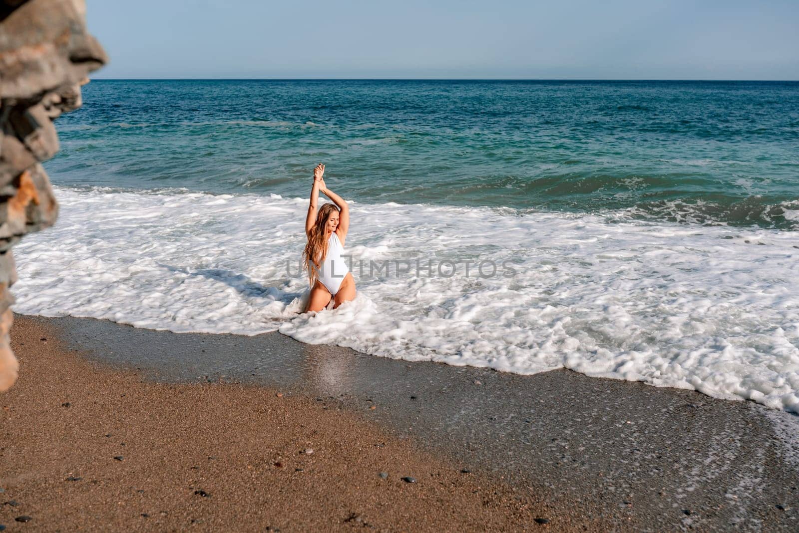 Happy woman in bikini sits on the sea beach. Tanned girl sunbathing on a beautiful shore. Summer vacation or holiday travel concept.