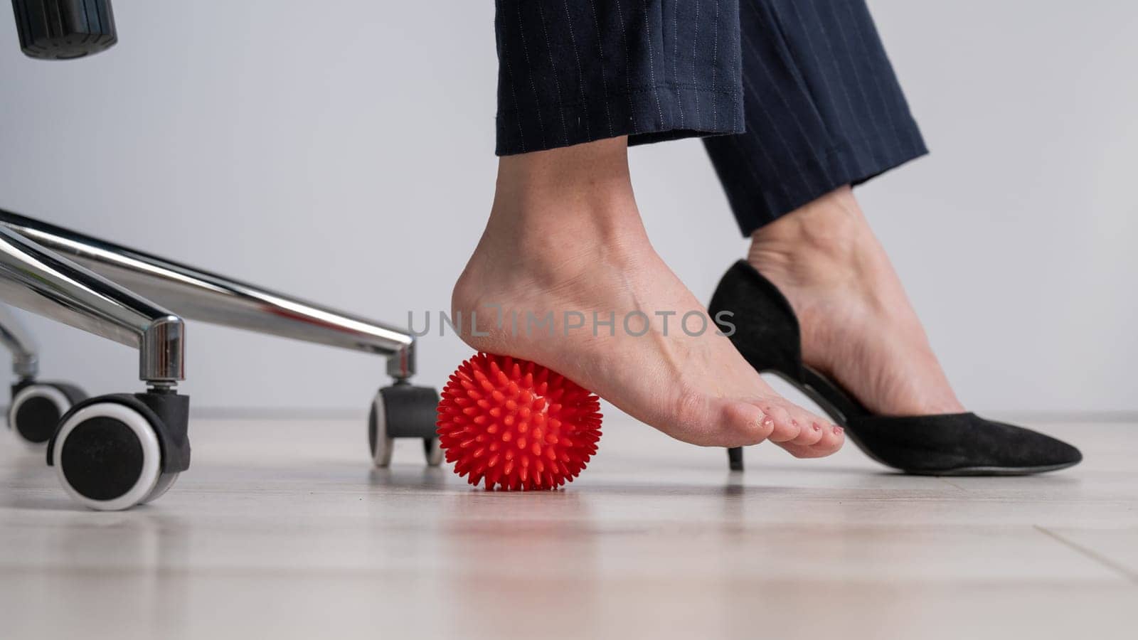 Business woman massages her feet on a massage ball with spikes. by mrwed54