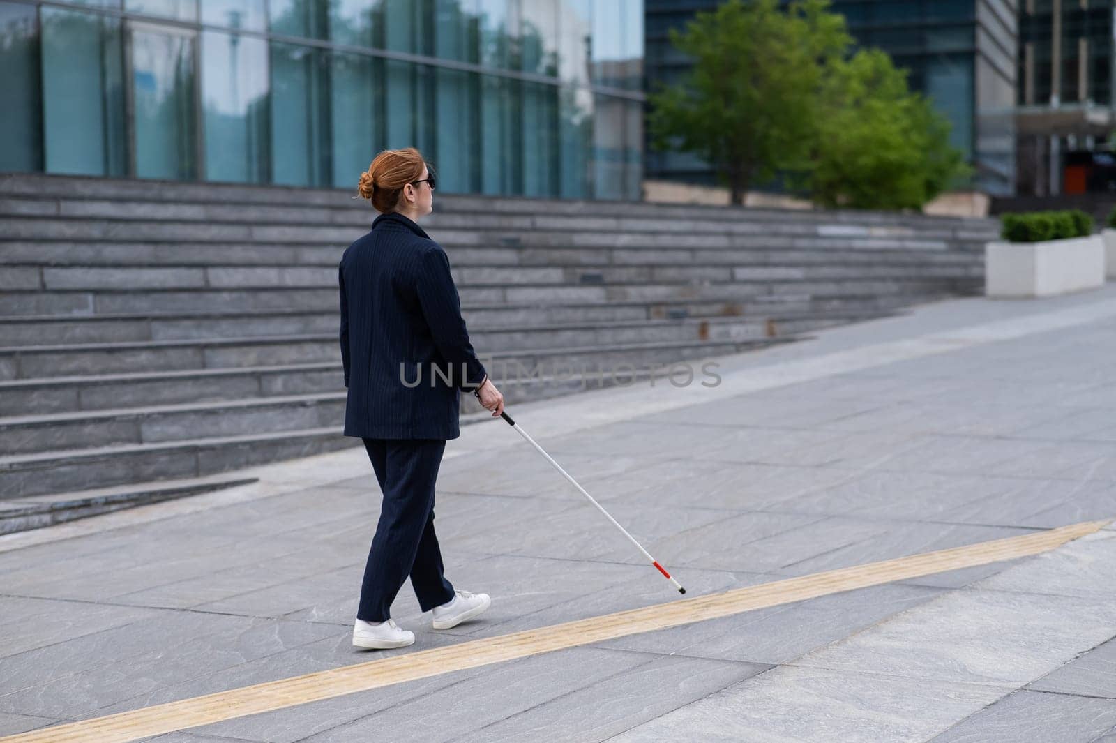 Blind businesswoman walking along tactile tiles with a cane