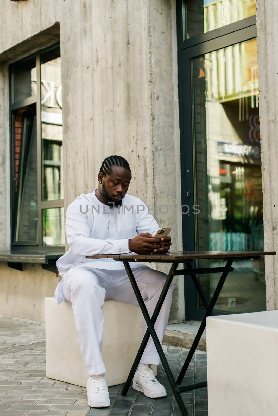 African american man checks cell phone in the street cafe in summer day. Millennial generation and gen z people. Social networks and dating app