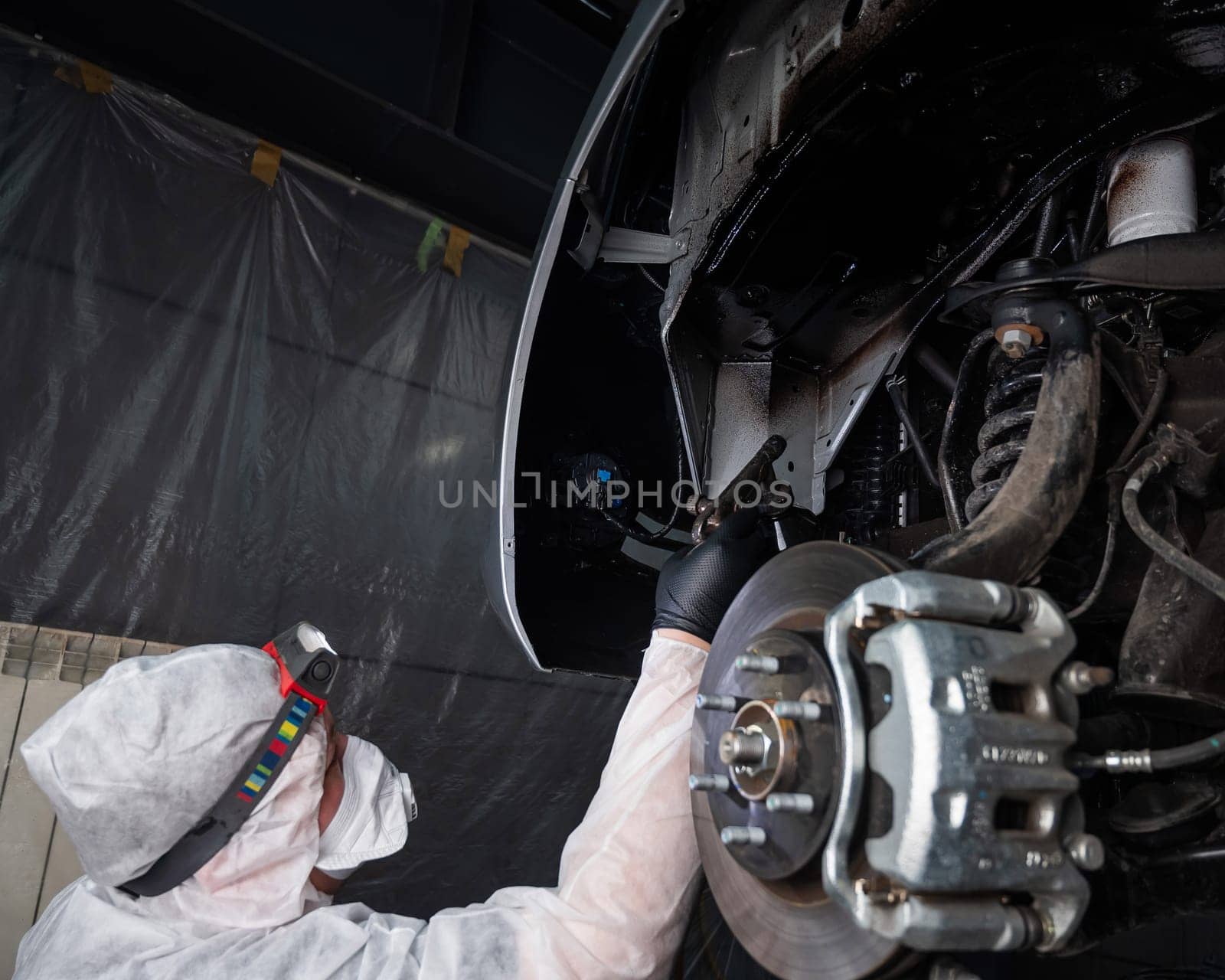 An auto mechanic applies anti-corrosion mastic to the underbody of a car. by mrwed54