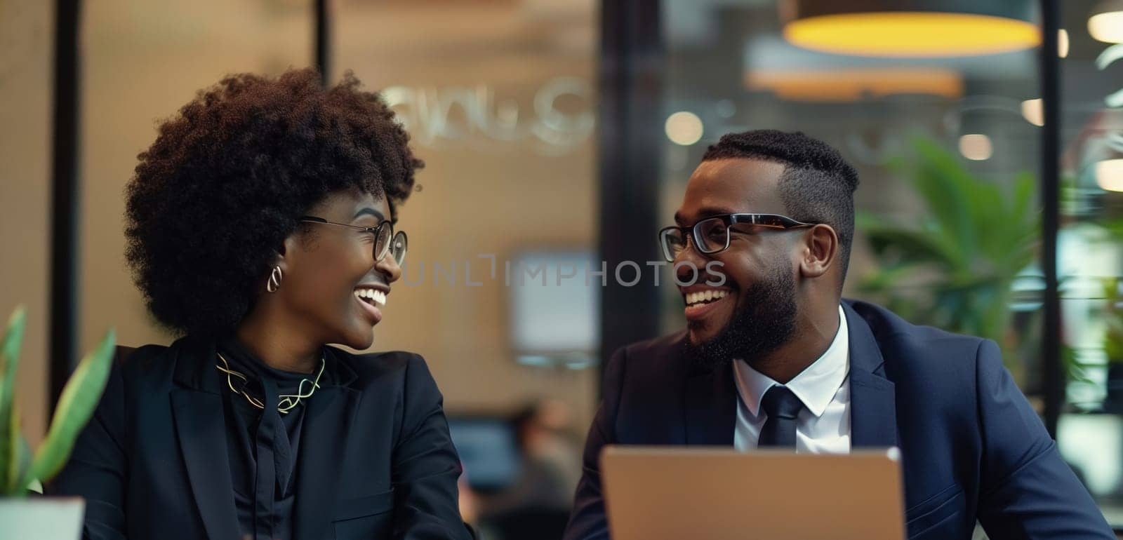 Happy smiling business people discussing a new project together sitting at the desk with laptop in an office, cheerful african colleagues having a conversation at a meeting