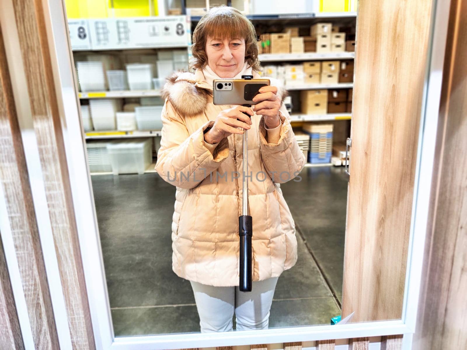 Middle-Aged Woman Shopping and Takes a selfie in the mirror at a Warehouse Store. Woman browsing in large retail store aisle