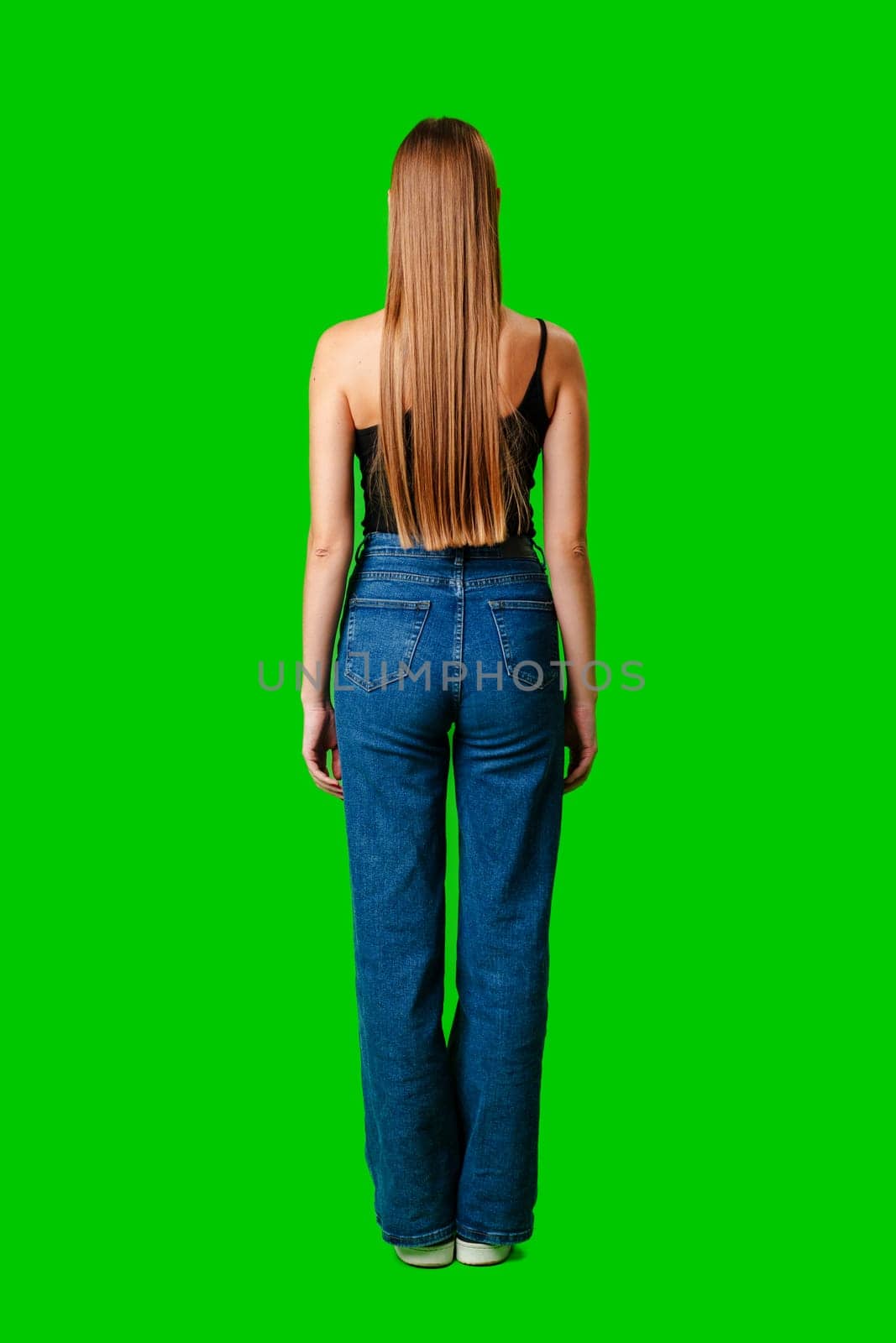 Woman in blue jeans with long hair on green background back view by Fabrikasimf