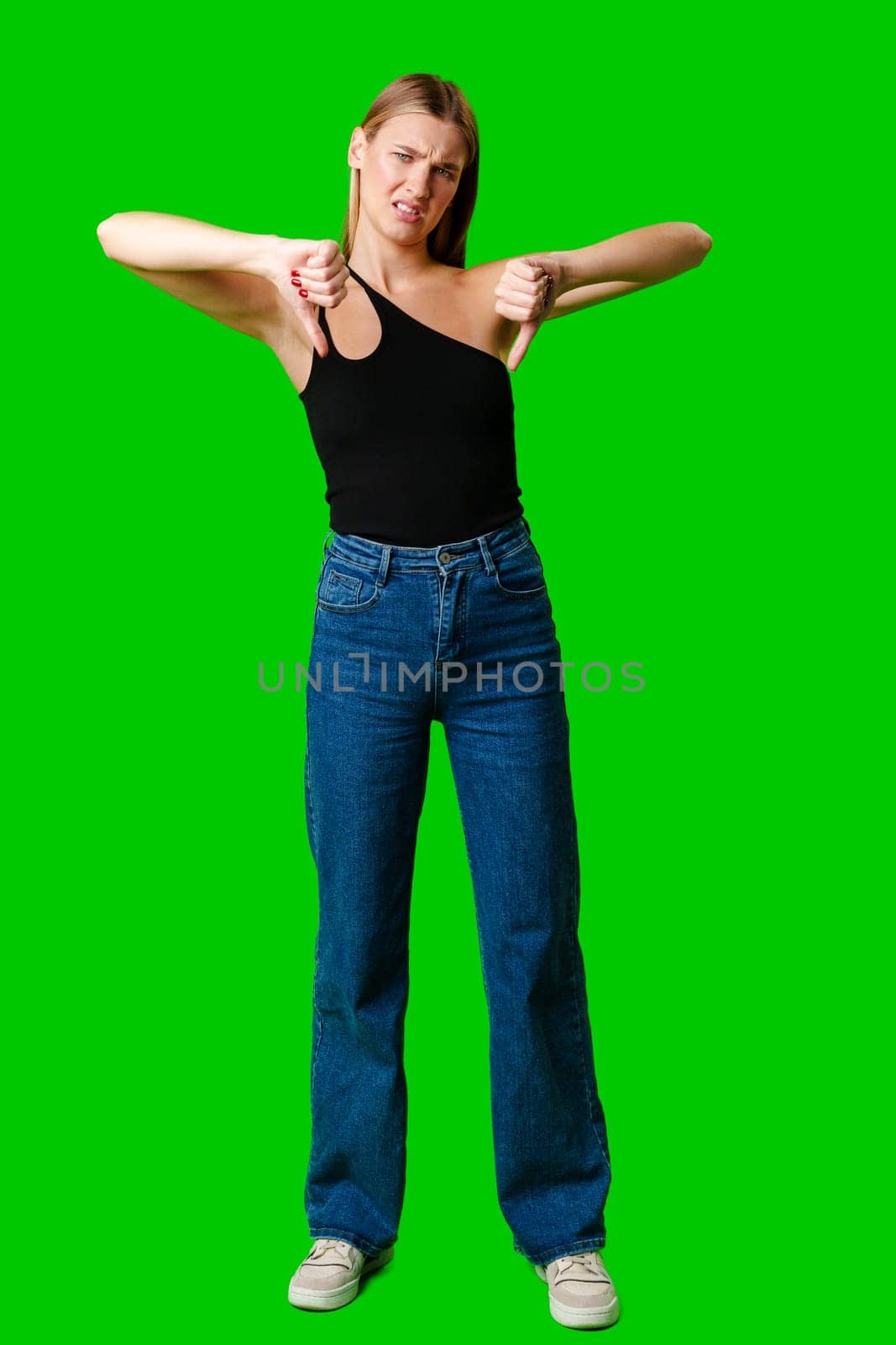 Young Woman Expressing Disapproval With a Thumbs Down Gesture Against a Green Background by Fabrikasimf