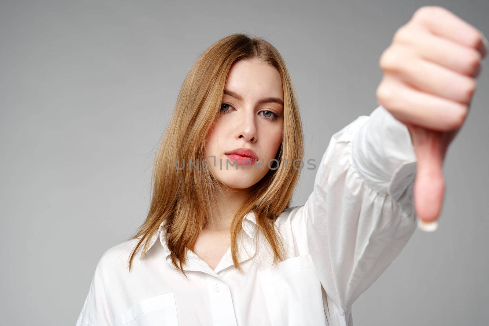 Young Woman in White Shirt Pointing Finger Down Dislike against gray background