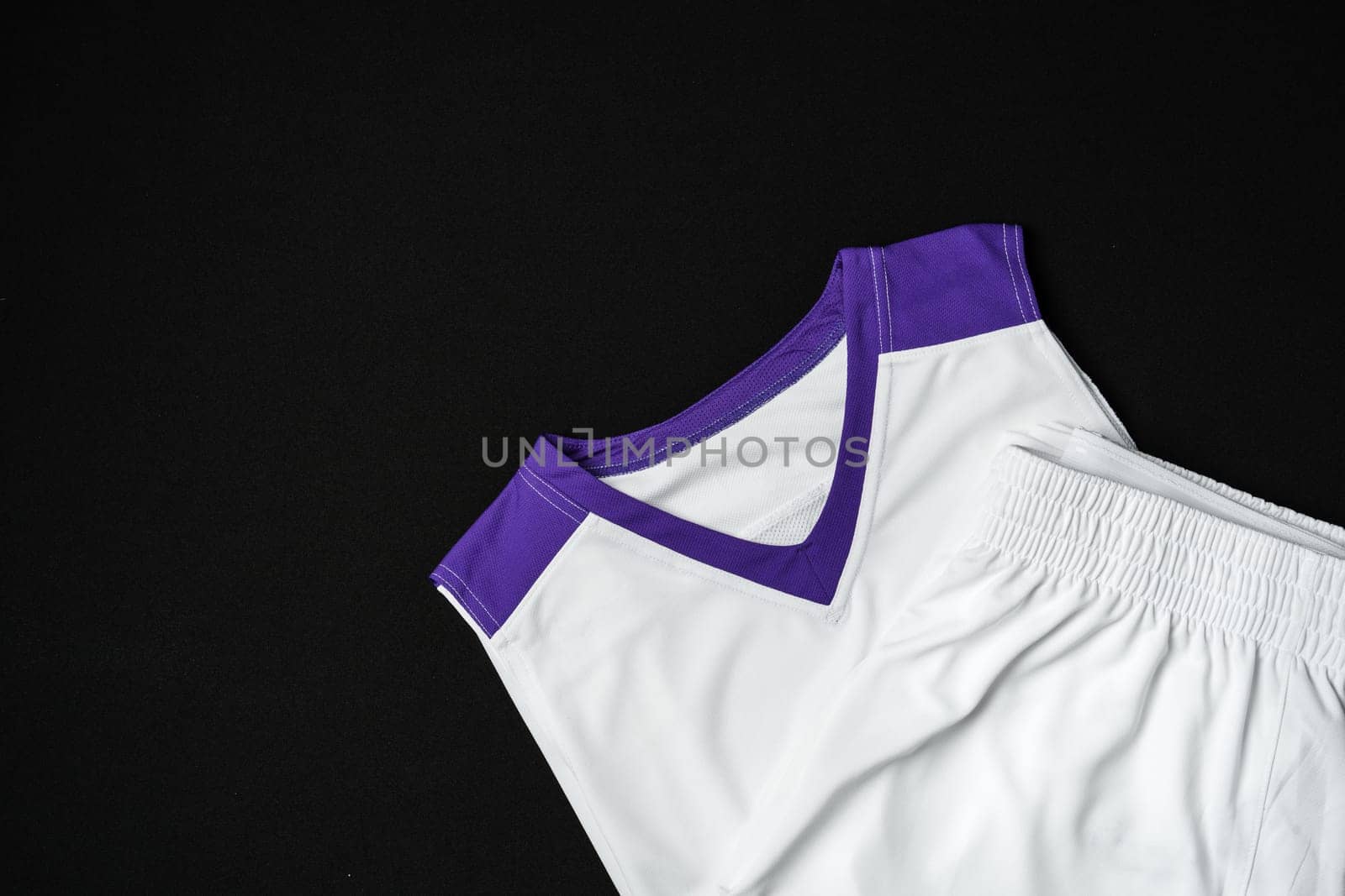 A close-up view of a white and purple athletic tank top neatly arranged on a dark background, highlighting its sporty design and contrasting vibrant trim. The fabric texture suggests a focus on breathability and performance, suitable for sportswear.