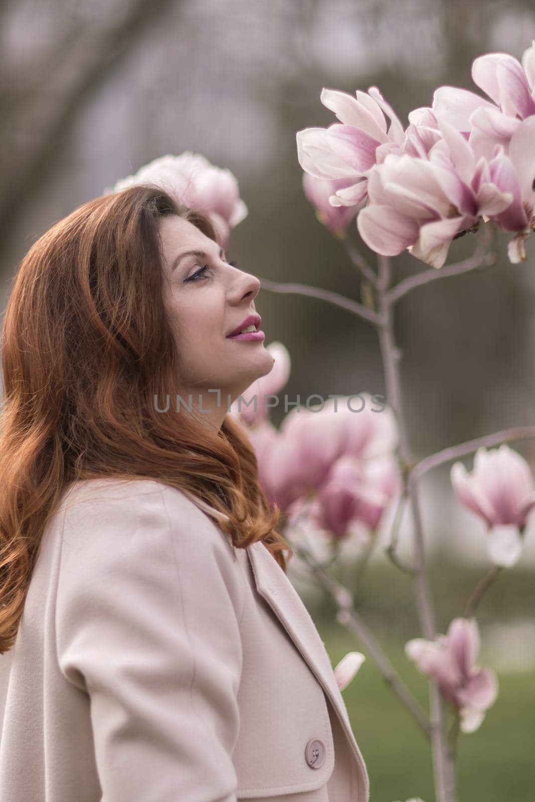 Woman magnolia flowers, surrounded by blossoming trees., hair down, wearing a light coat. Captured during spring, showcasing natural beauty and seasonal change. by Matiunina