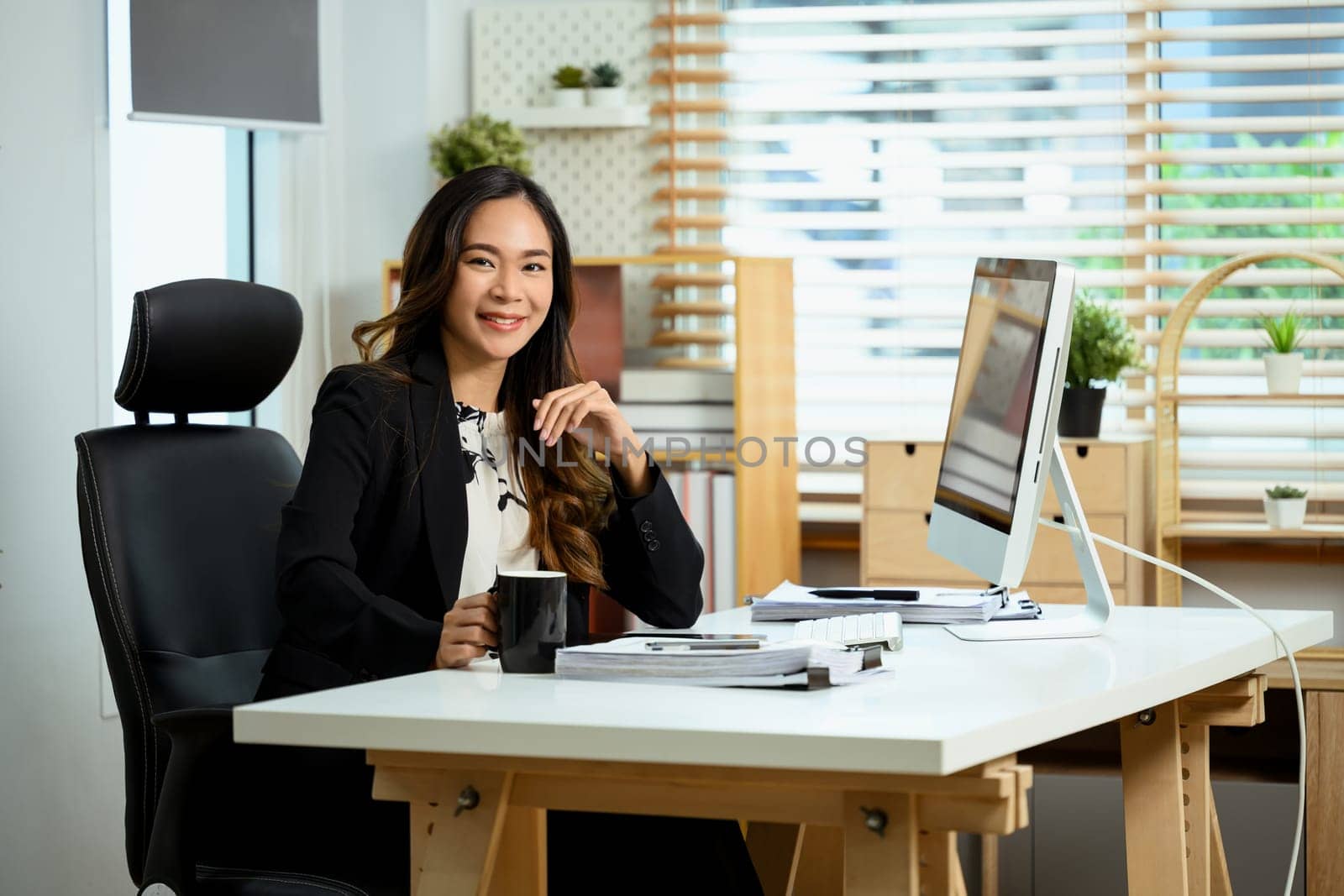 Confident millennial businesswoman sitting at working desk and smiling at camera.