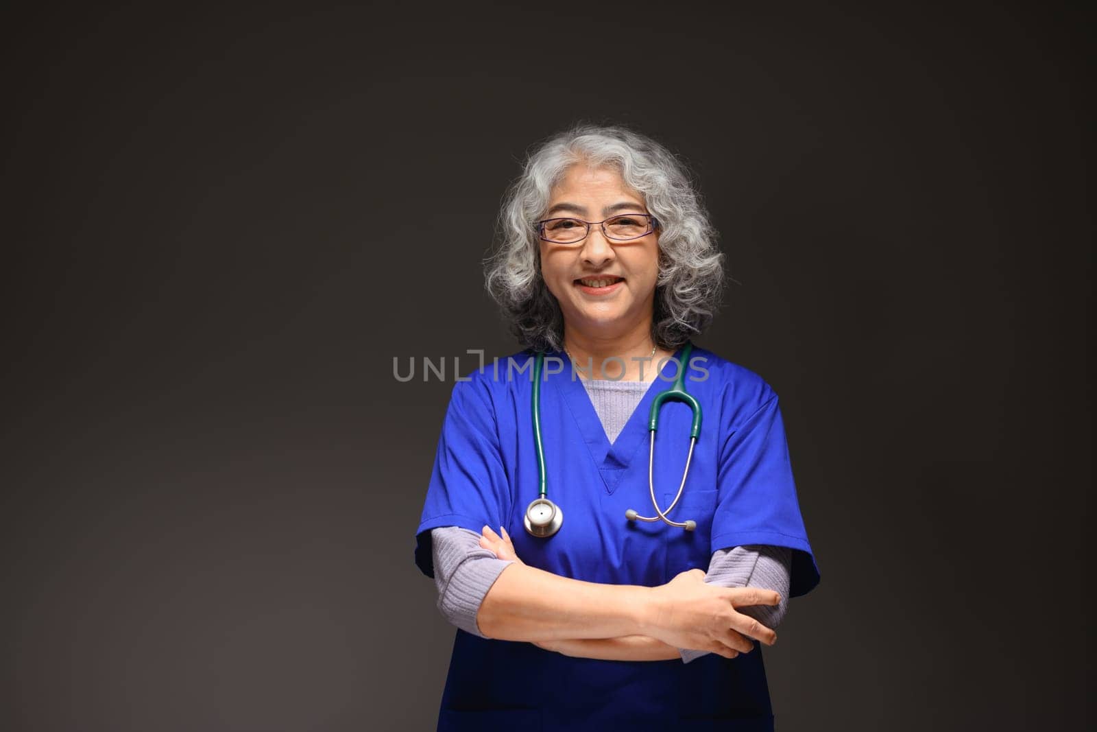 Portrait of friendly mature female doctor with stethoscope around her neck standing on black background.