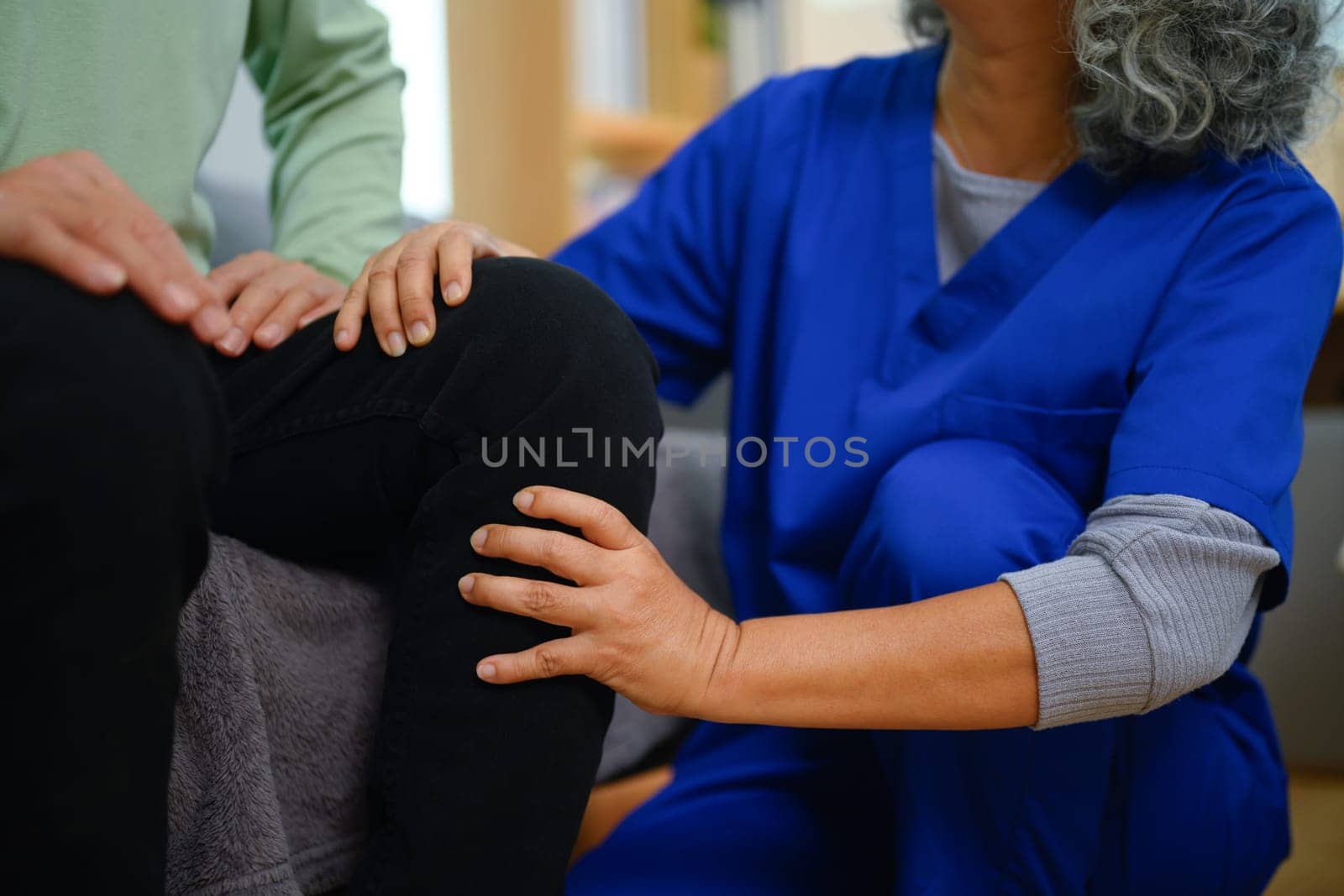 Female physiotherapist giving leg massage to senior man at home. Healthcare concept by prathanchorruangsak