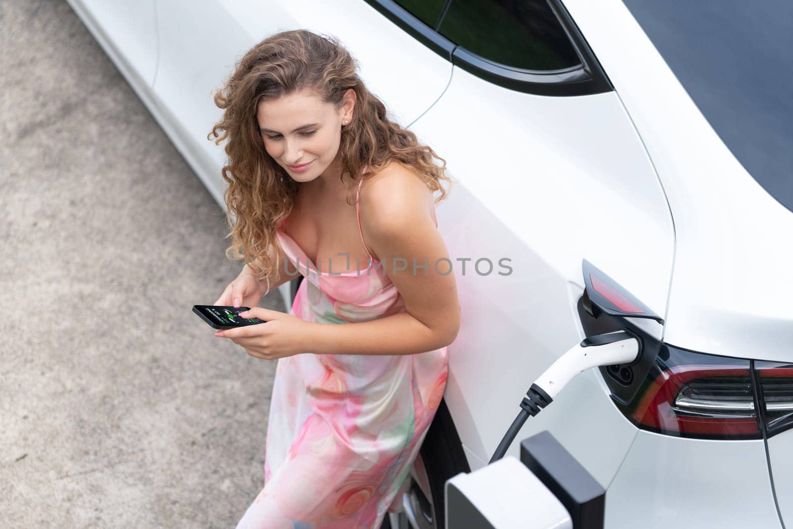 Modern eco woman recharge EV car with smartphone. Synchronos by biancoblue