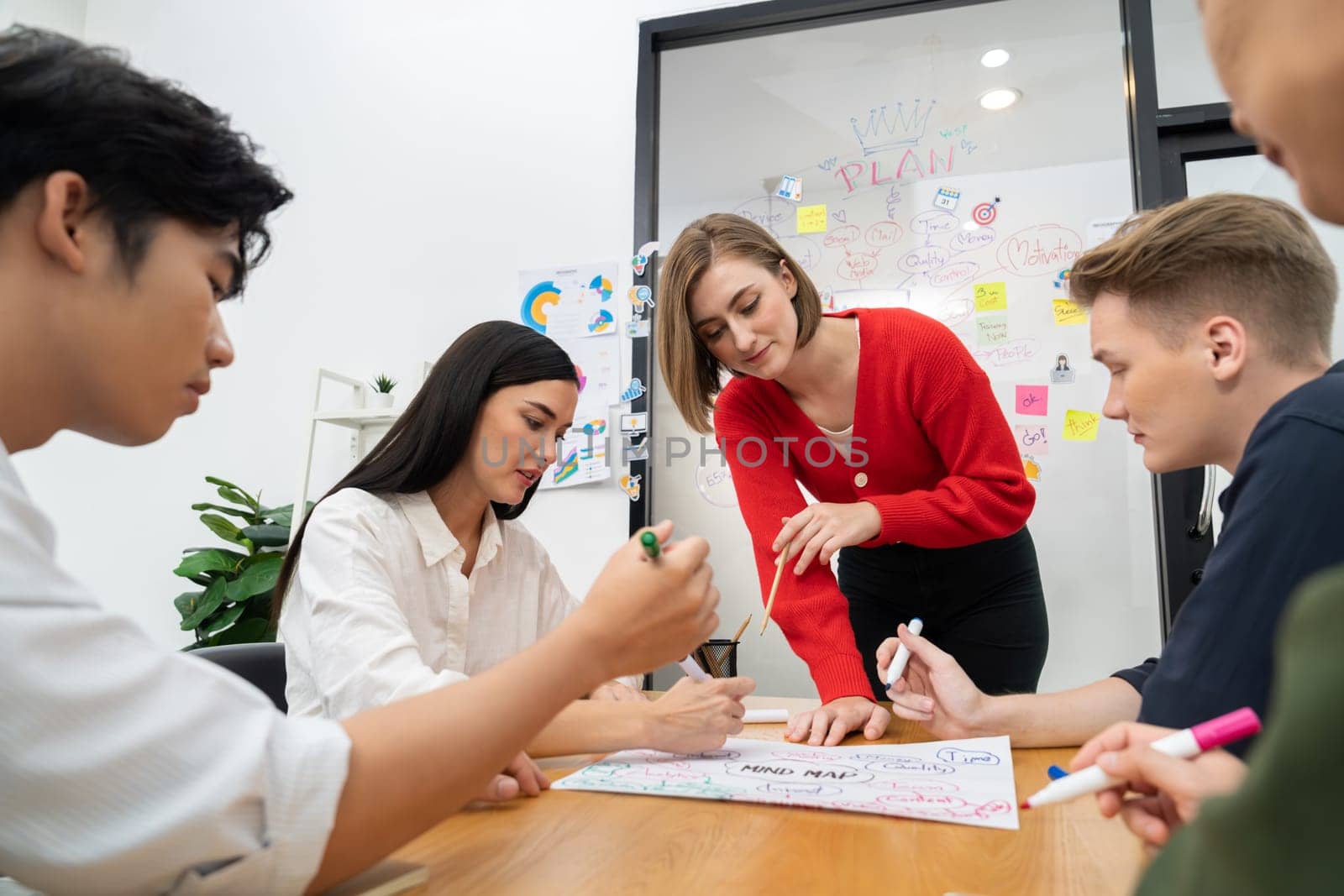 Creative happy business team brainstorming and sharing idea by using mind map and graphic graph while young beautiful project manager pointing at important point at business meeting. Immaculate.