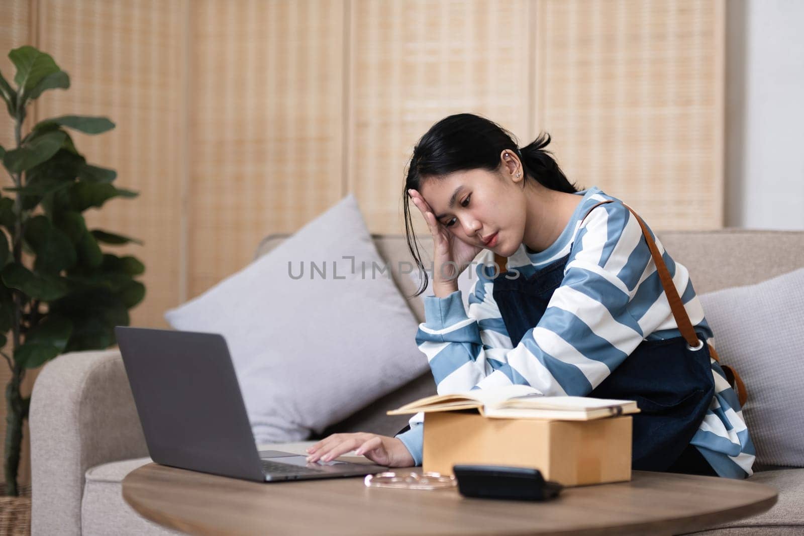 A small SME business owner feels tired while sitting on his home desk packing products into boxes. by wichayada