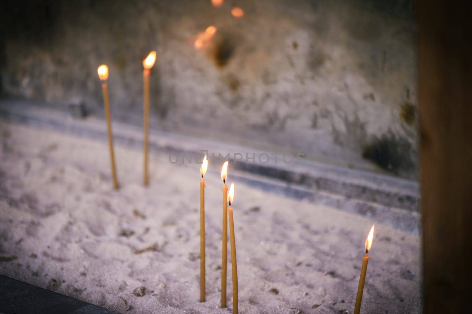 Scattered candles glowing with a golden yellow light in the sand, copy space