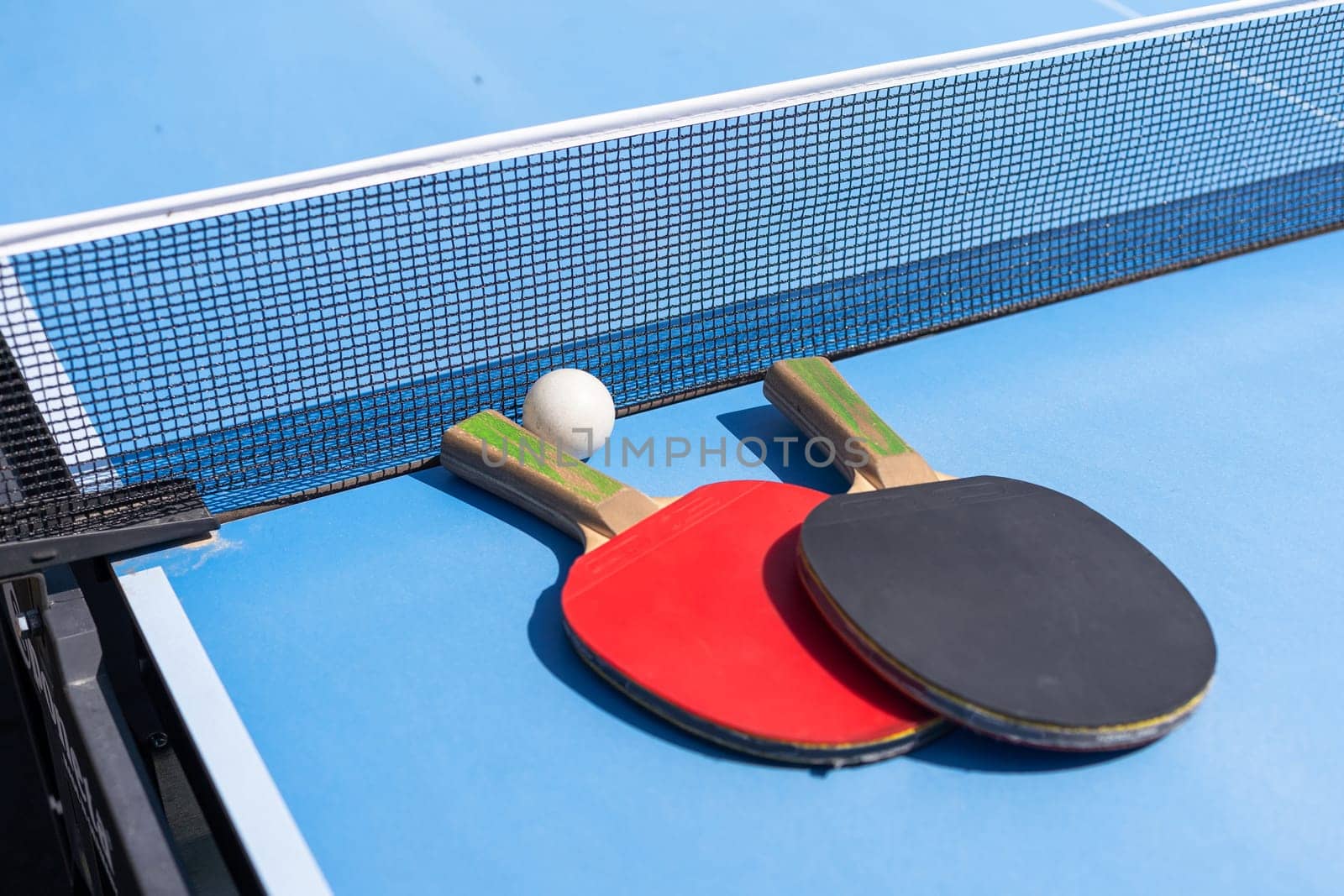 Red and black Table Tennis Paddles and ball on the blue table tennis table with net. Ping Pong concept with copy space. High quality photo