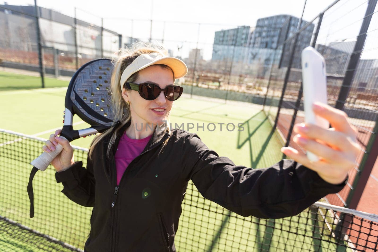 Young female smiling and looking at camera while playing padel against green background. High quality photo