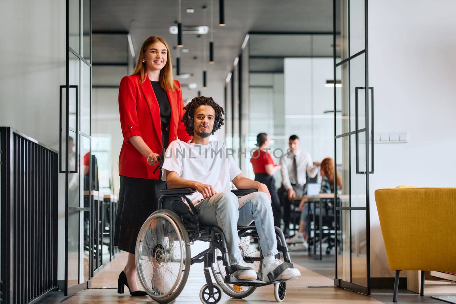 A business leader with her colleague, an African-American businessman who is a disabled person, pass by their colleagues who work in modern offices by dotshock