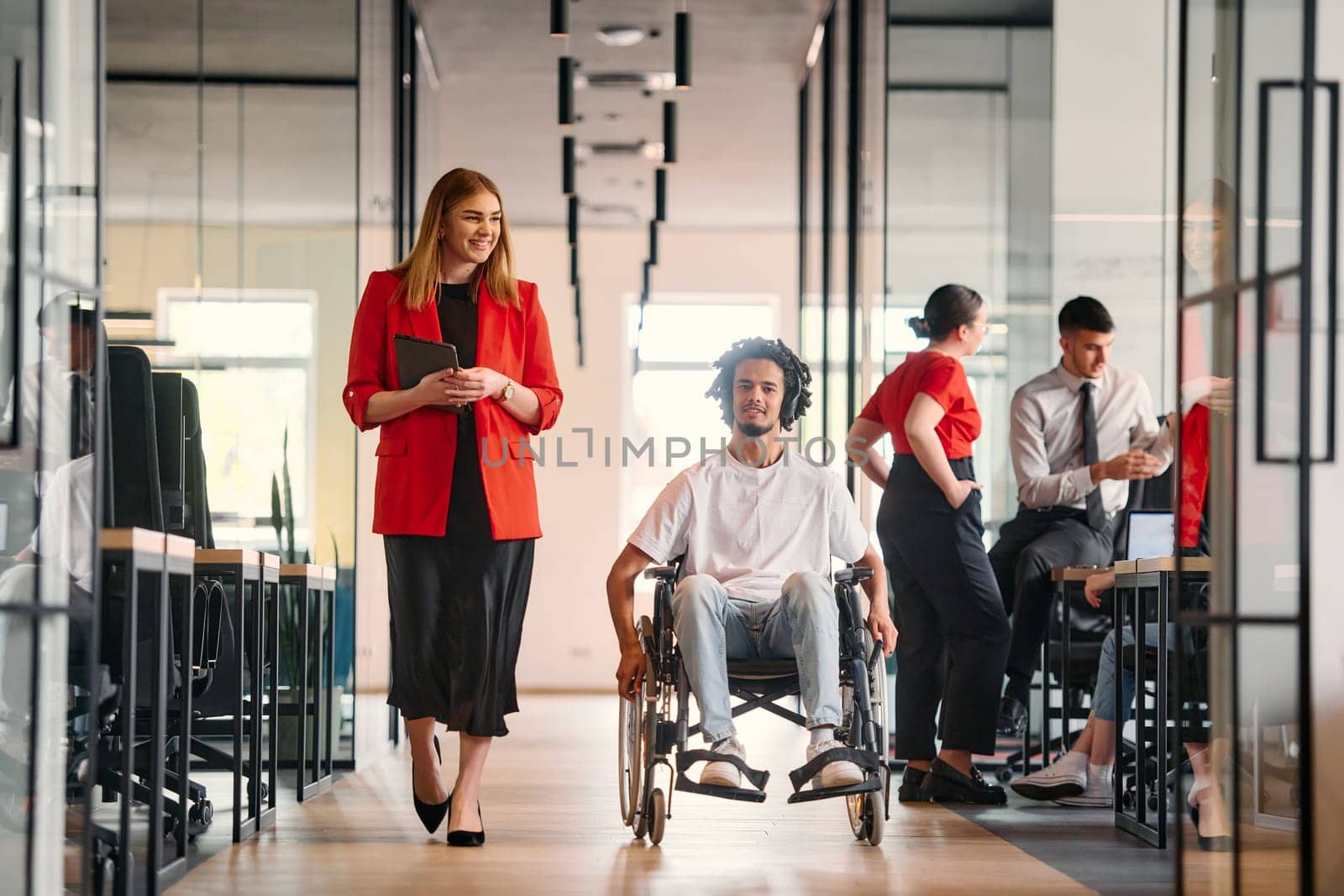 A business leader with her colleague, an African-American businessman who is a disabled person, pass by their colleagues who work in modern offices by dotshock