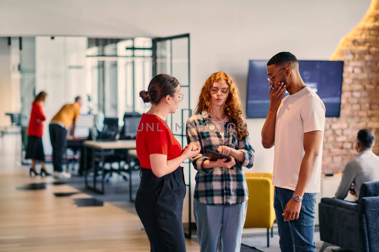 A group of young business individuals, including a girl with orange hair and an African American man, stands in a modern corporate hallway, collectively examining business progress on a smartphone, exemplifying dynamic collaboration and digital engagement. by dotshock