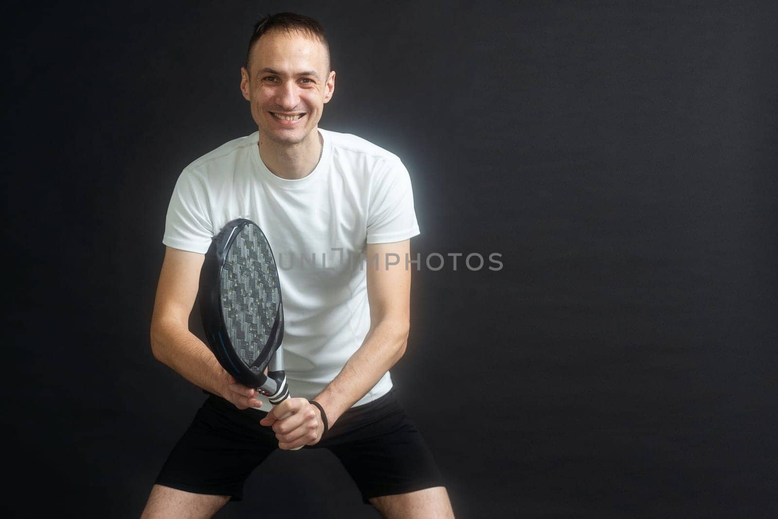 Portrait of man playing paddle tennis in position to hit a backhand ball black isolated background. Front view. High quality photo