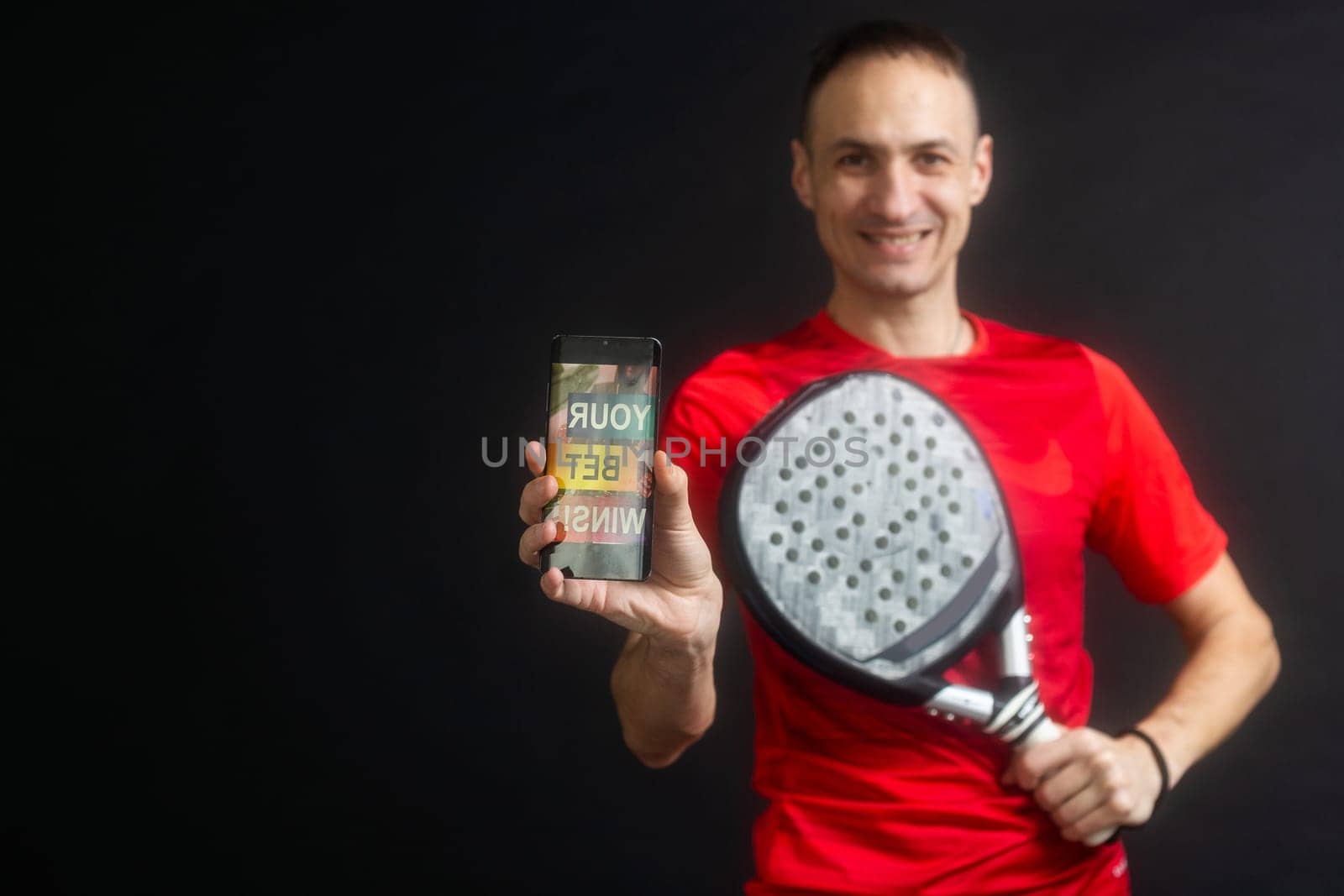 man holding paddel racket and smartphone with bet black background by Andelov13