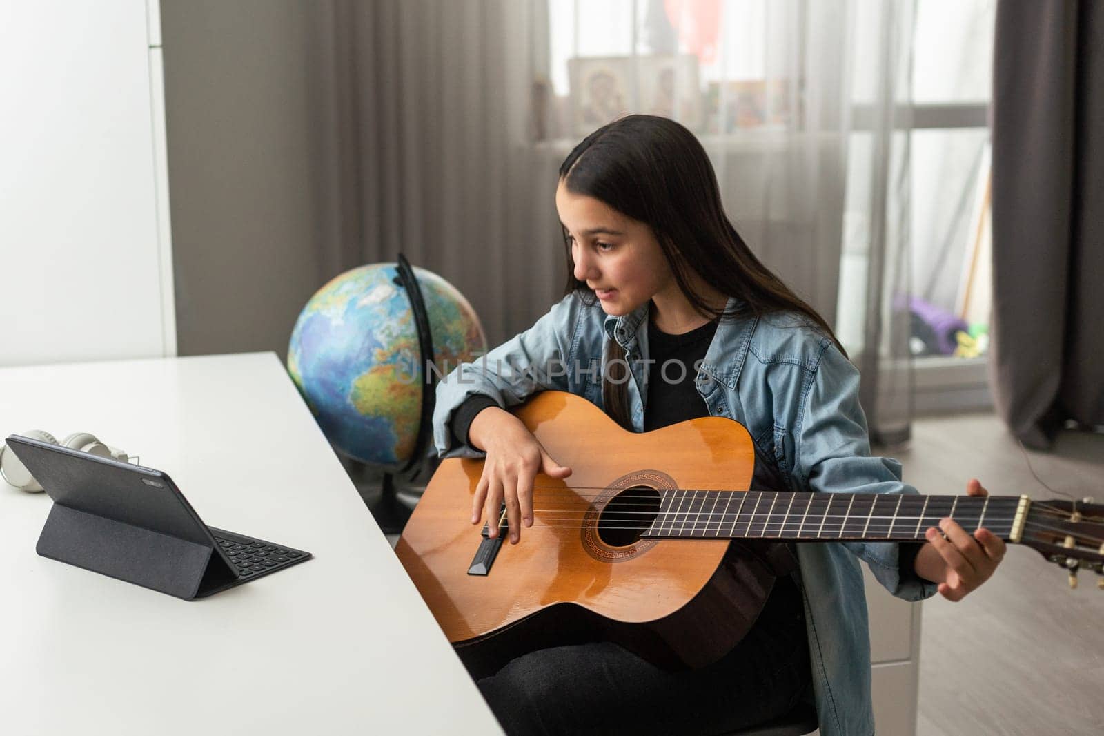 Beautiful young girl with long hair playing the guitar, sitting at home. studying the melody. Home leisure, hobbies, self-development. by Andelov13