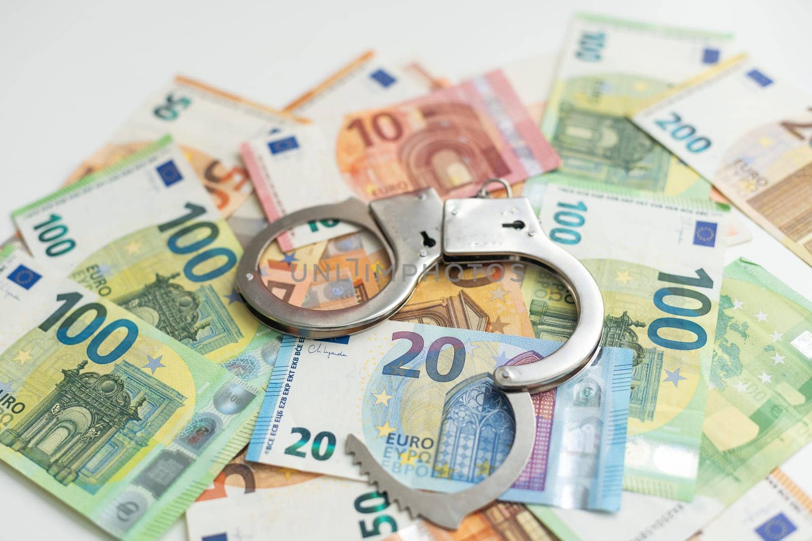 Police handcuffs lies on a set of green monetary denominations of 100 euros. A lot of money forms an infinite heap. High quality photo
