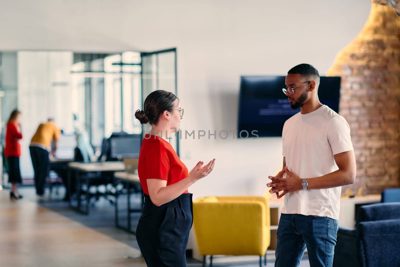 Young business colleagues, including an African American businessman, engage in a conversation about business issues in the hallway of a modern startup coworking center