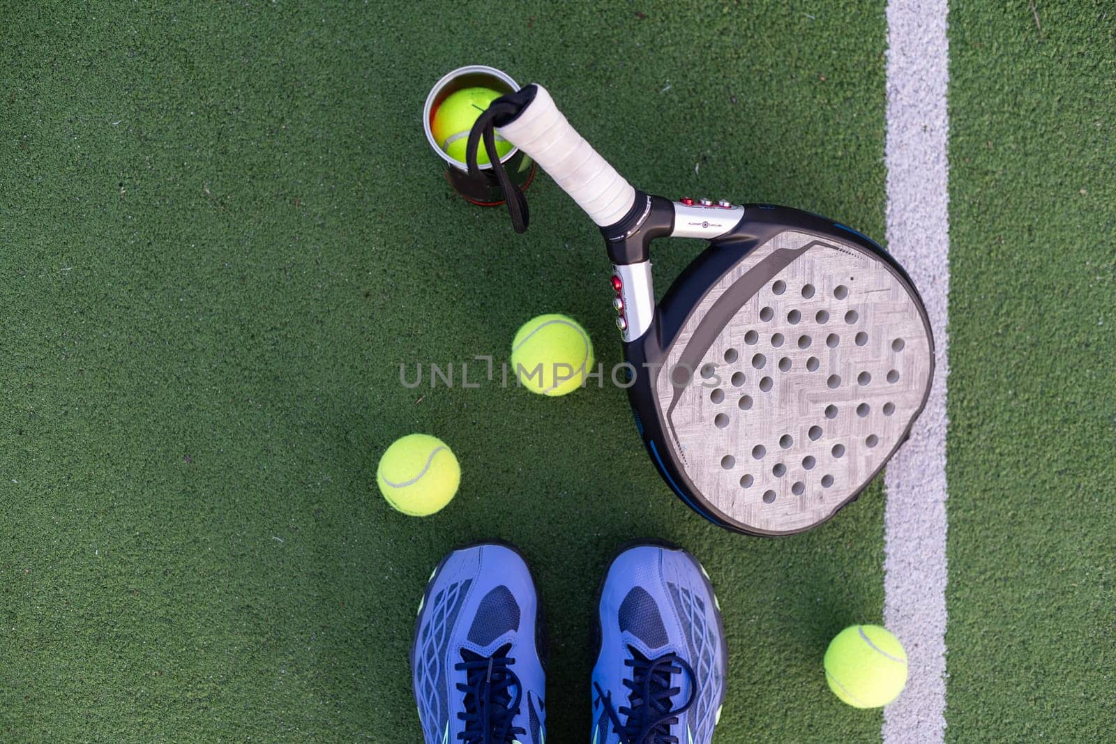Yellow balls on grass turf near padel tennis racket behind net in green court outdoors with natural lighting. Paddle is a racquet game. Professional sport concept with copy space. High quality photo