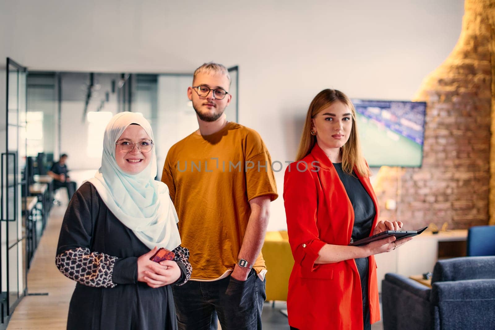 A group of young business colleagues, including a woman in a hijab, stands united in the modern corridor of a spacious startup coworking center, representing diversity and collaborative spirit. by dotshock