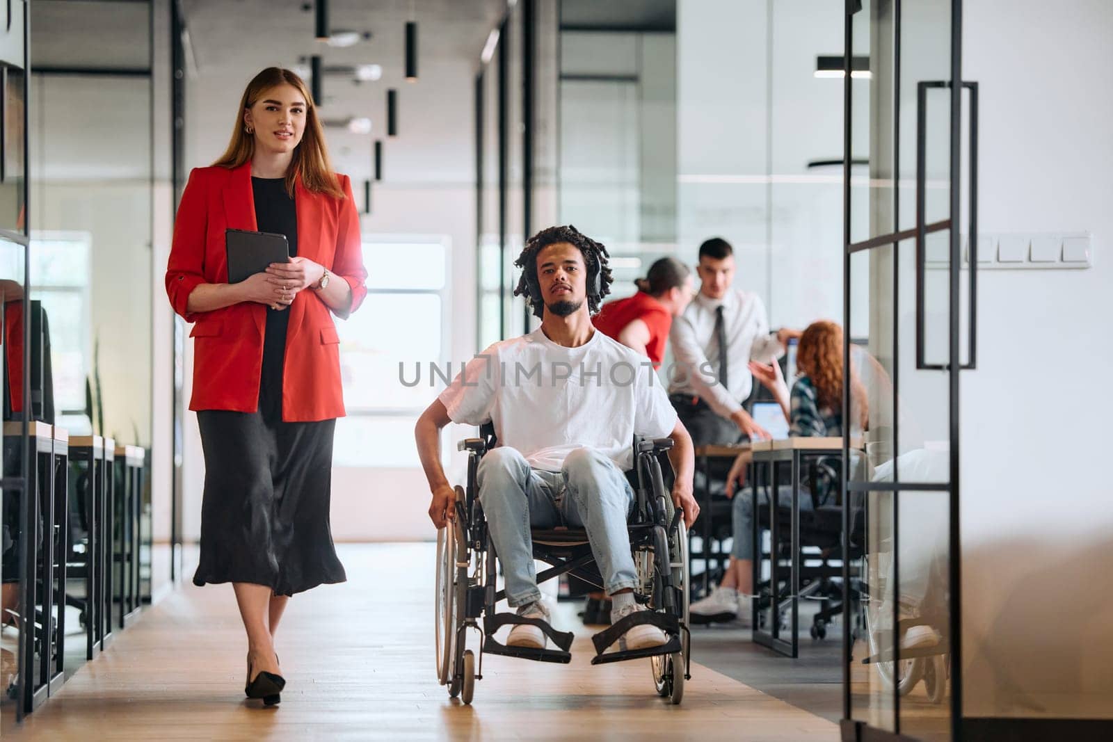 A business leader with her colleague, an African-American businessman who is a disabled person, pass by their colleagues who work in modern offices by dotshock