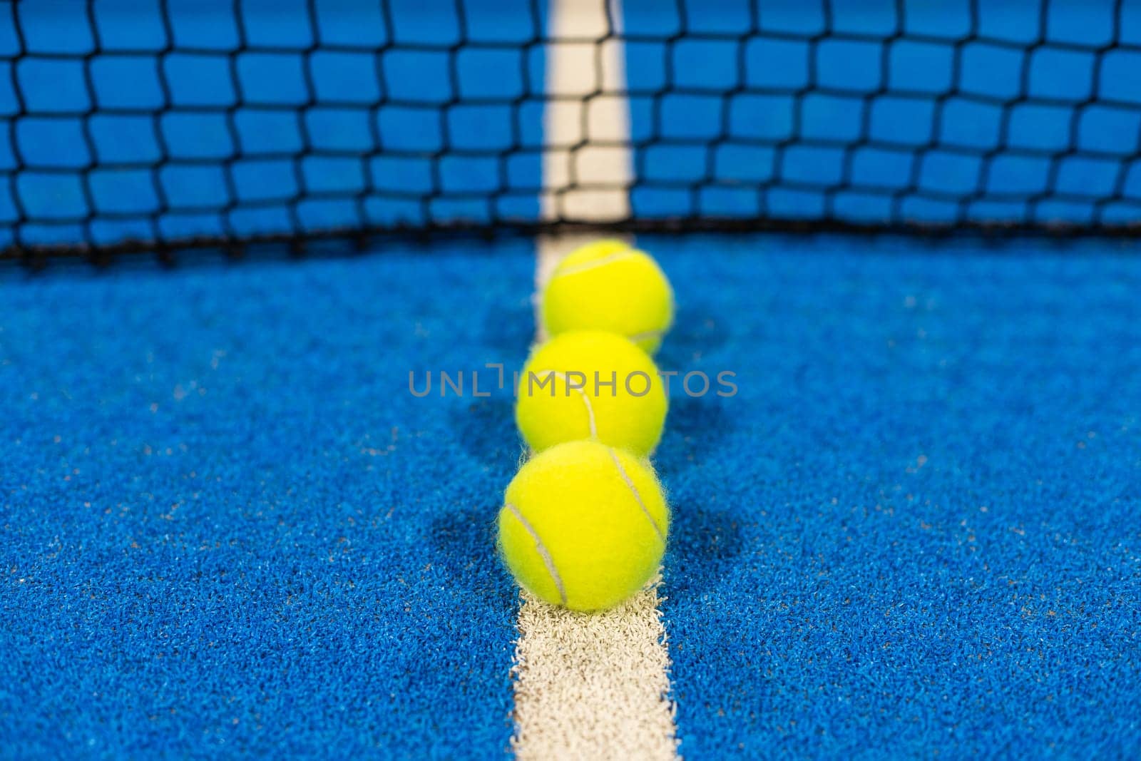 several balls by the net on a blue paddle tennis court. High quality photo