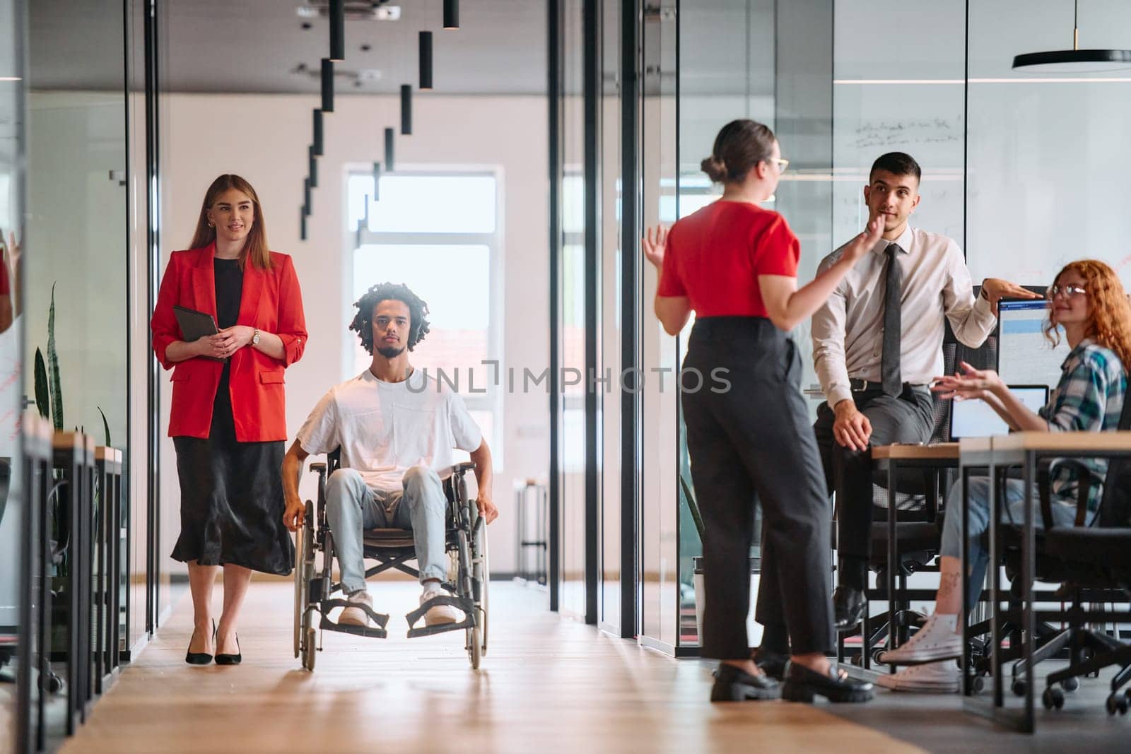 A business leader with her colleague, an African-American businessman who is a disabled person, pass by their colleagues who work in modern offices by dotshock