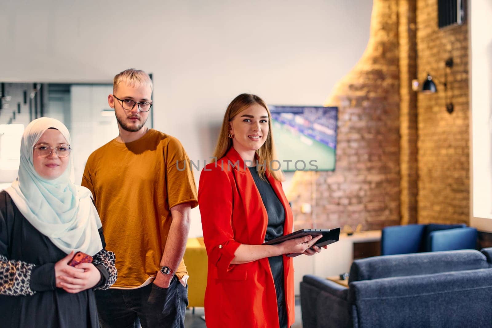 A group of young business colleagues, including a woman in a hijab, stands united in the modern corridor of a spacious startup coworking center, representing diversity and collaborative spirit. by dotshock