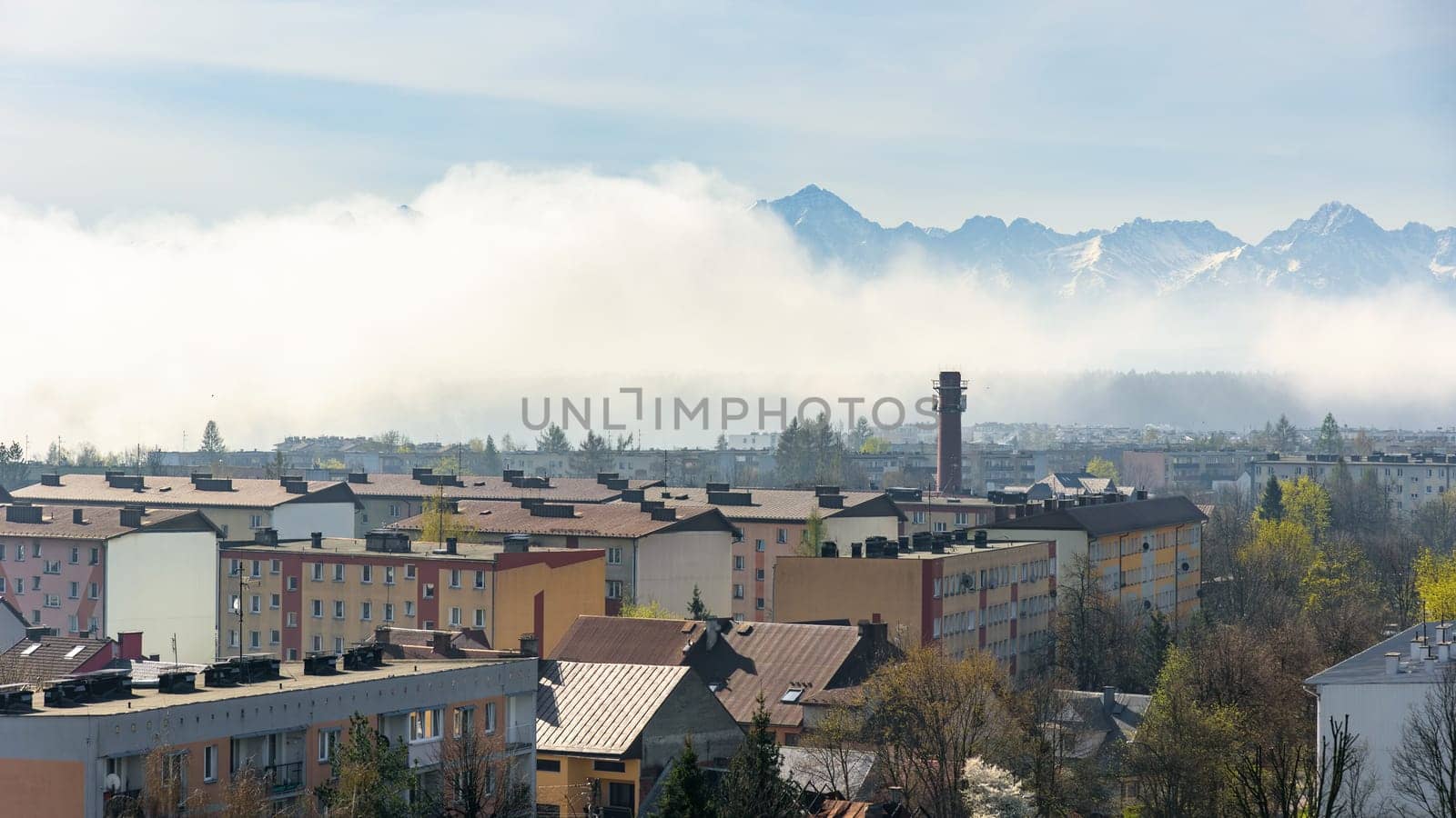 Panoramic view of the rooftops of Nowy Targ with snow capped Tatra mountains revealing from the morning fog