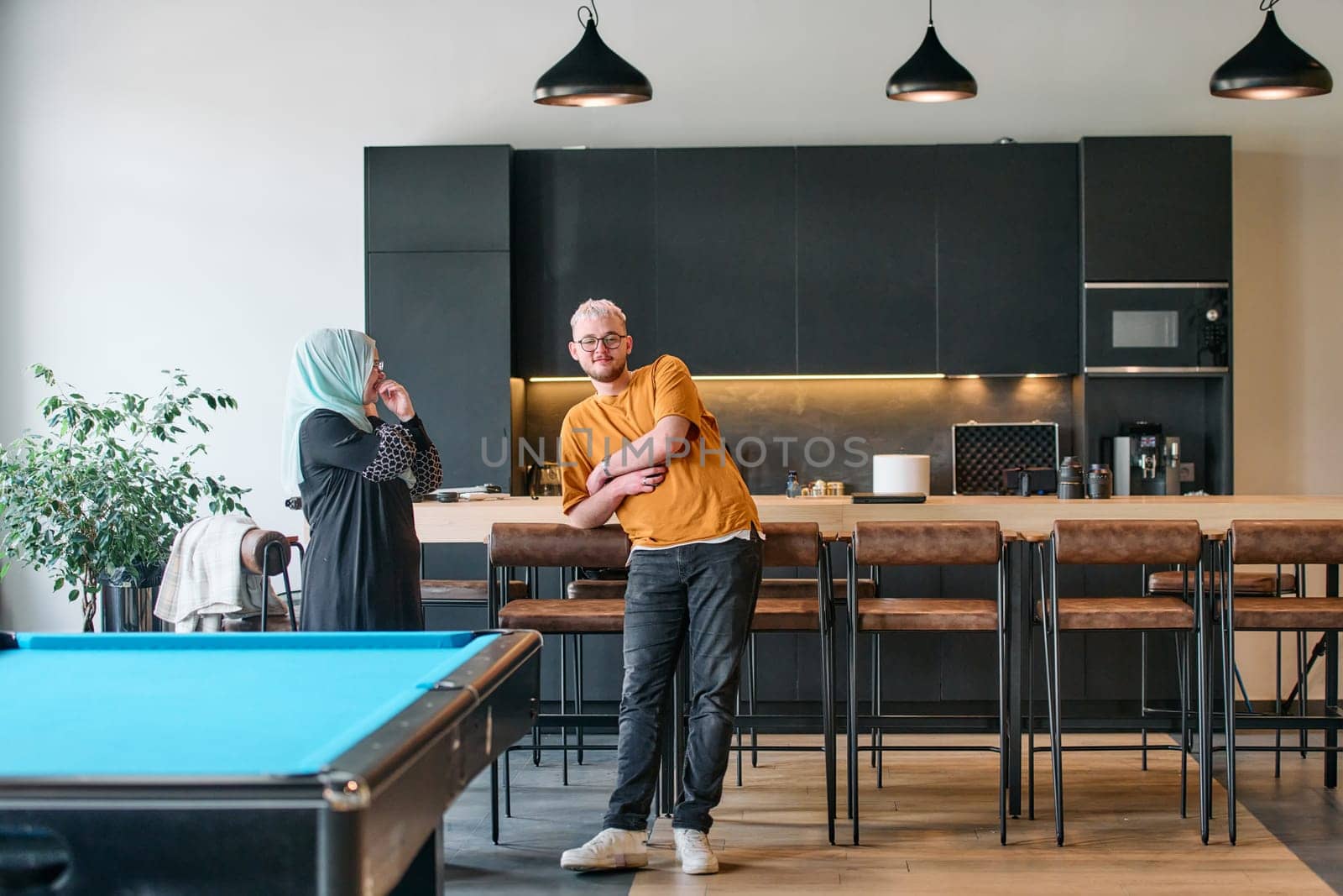 A candid moment captured in the workplace. A blonde man engages in conversation with his hijab clad female colleague during a coffee break