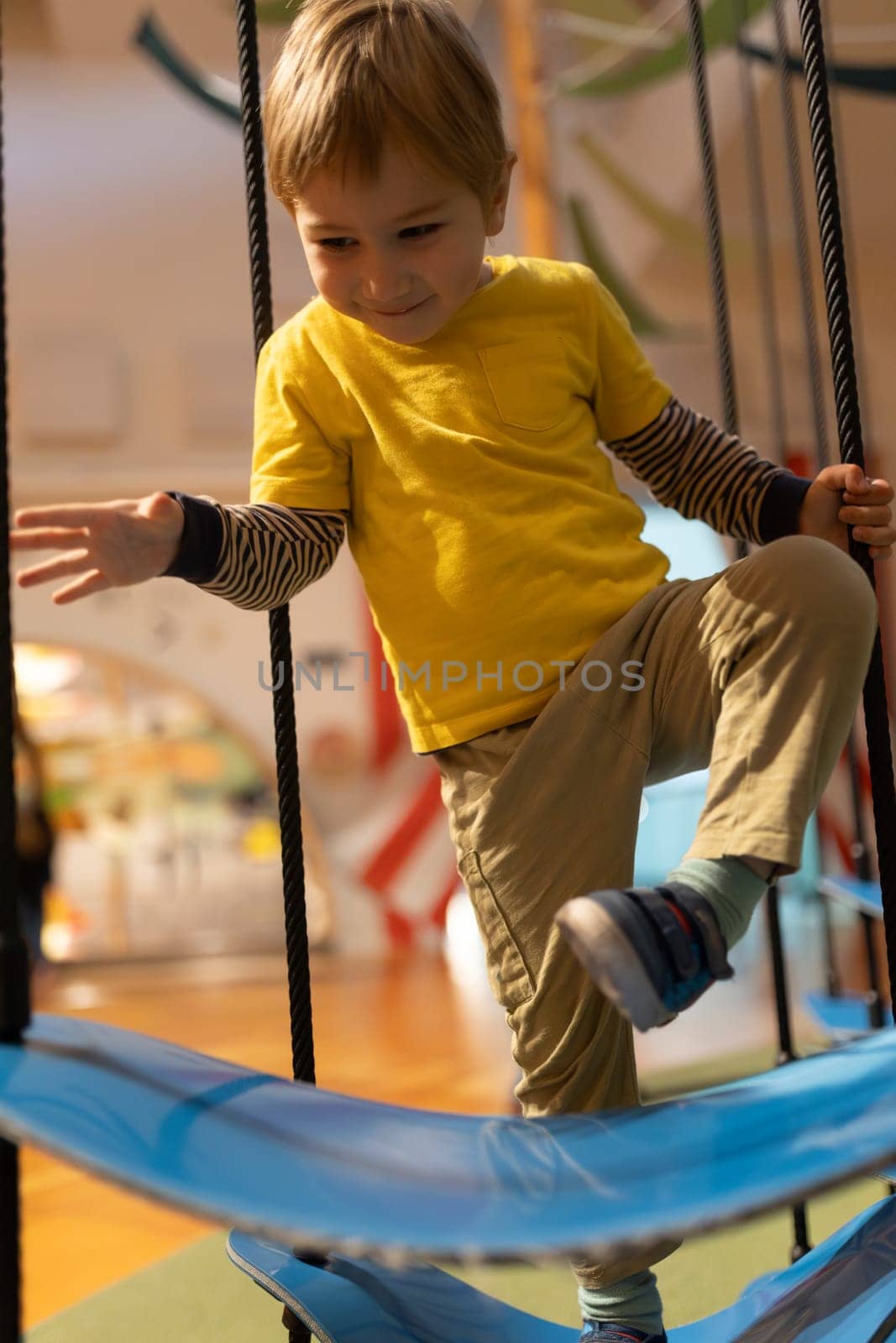 A young boy is playing on a swing set. He is wearing a yellow shirt and khaki pants