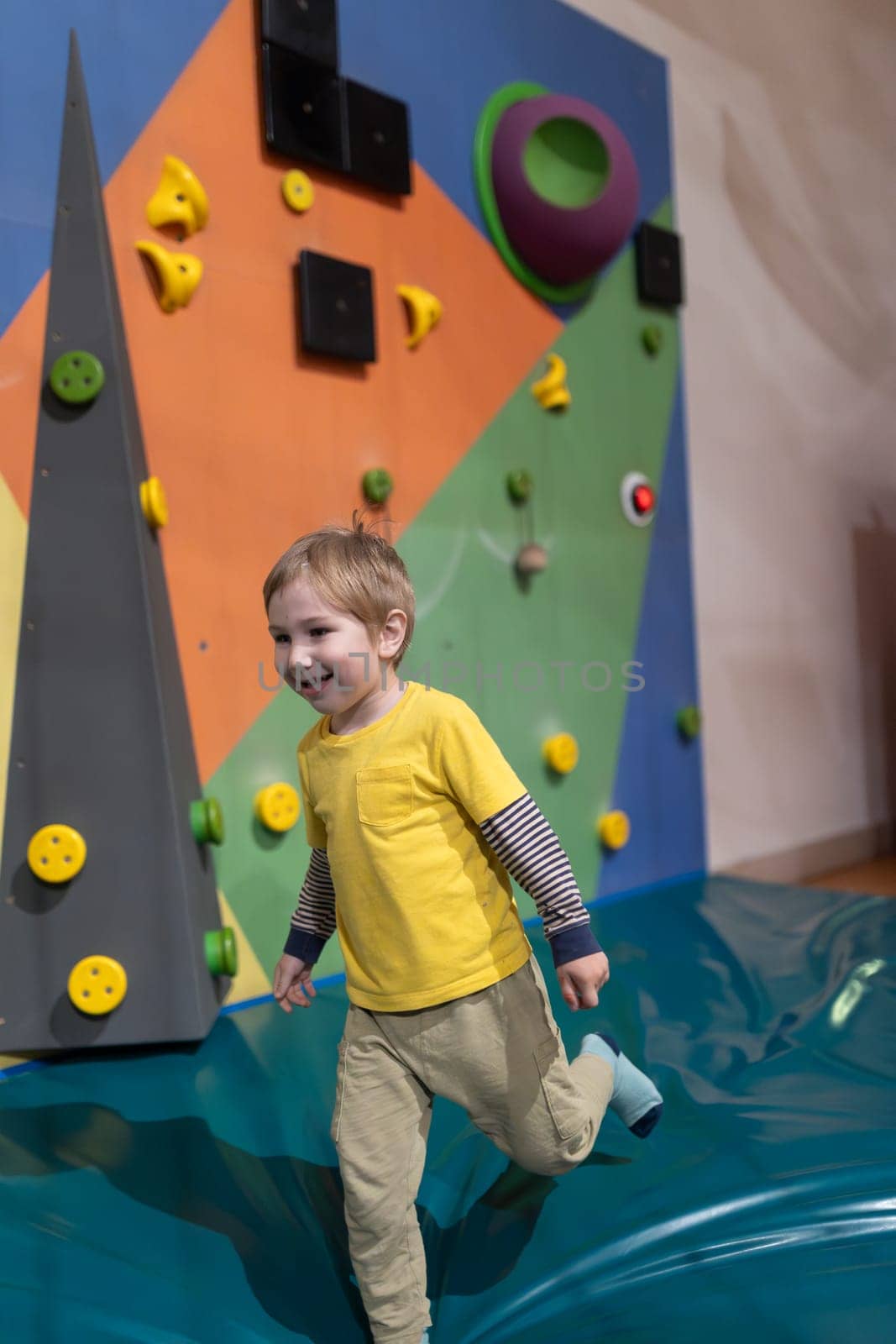 A young boy is running on a blue surface with a yellow shirt on by Studia72