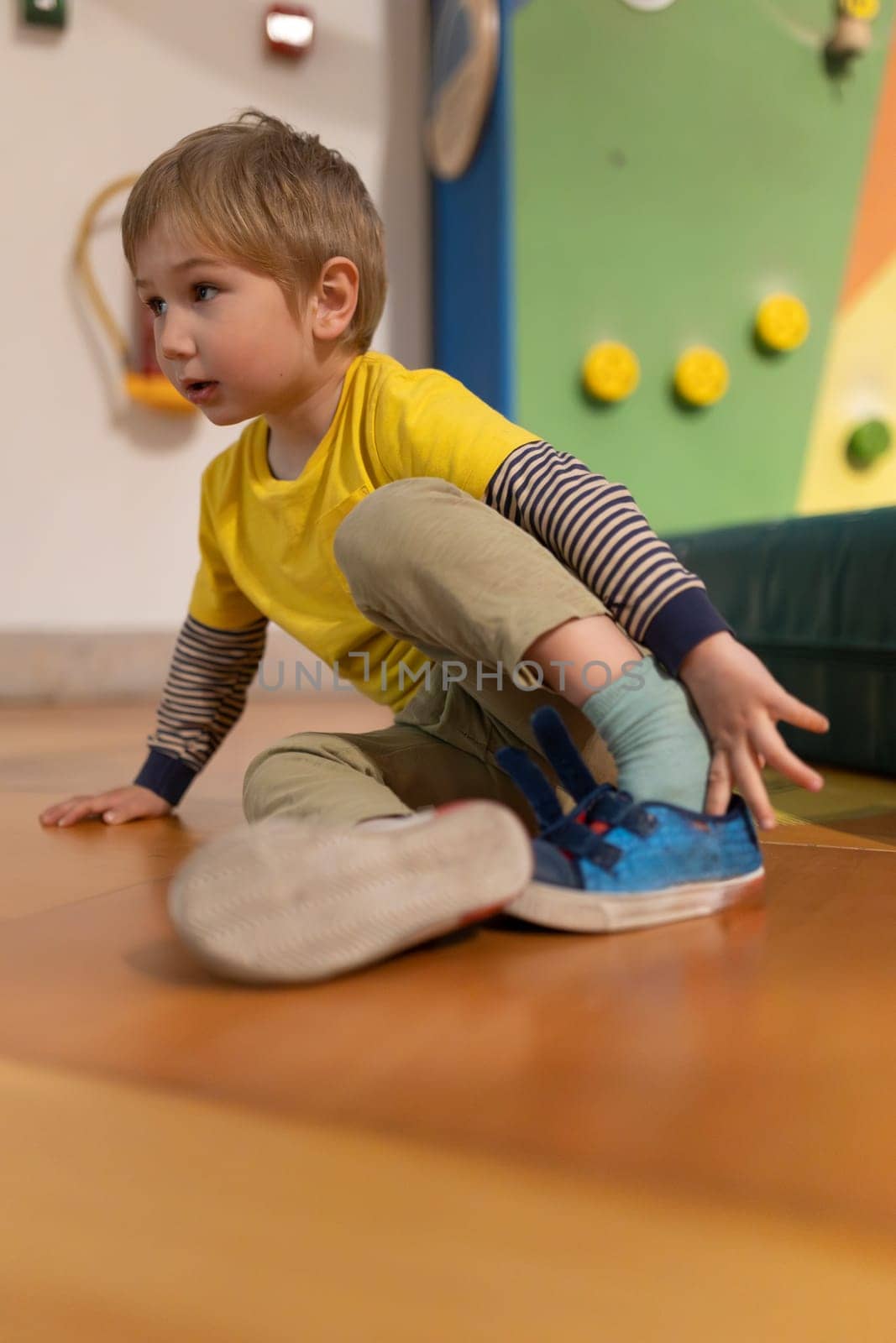 A young boy is sitting on the floor with his feet up. He is wearing a yellow shirt and blue shoes