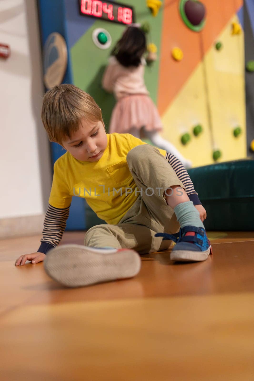 A boy in a yellow shirt is sitting on the floor with his feet up. He is wearing blue shoes