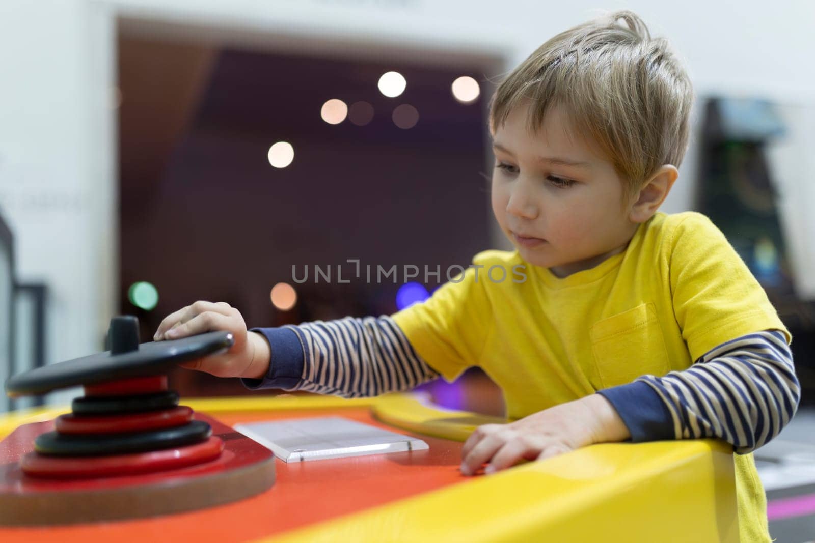 A young boy is playing a video game with a red button. The boy is wearing a yellow shirt and has a serious expression on his face