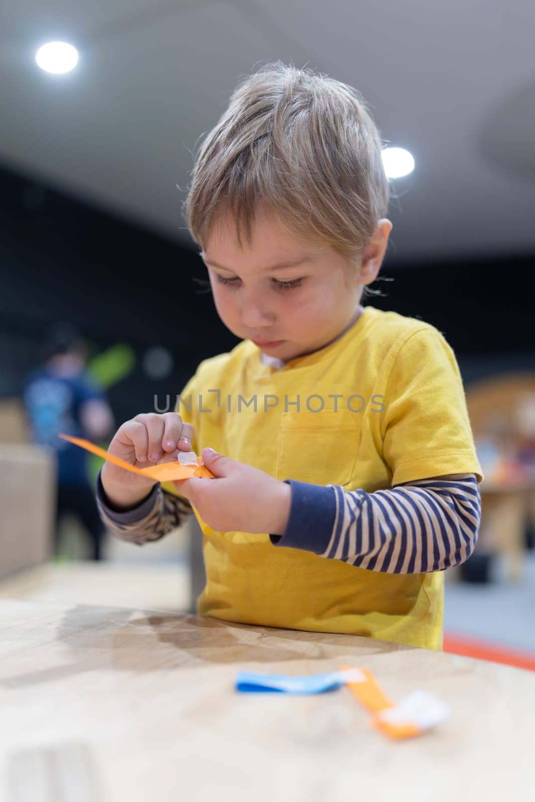 A young boy is sitting at a table, cutting paper with scissors by Studia72